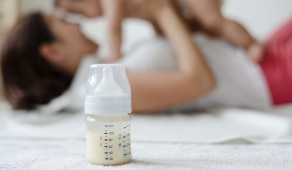 Baby formula with mom and baby in the background flesvoeding onder mama's
