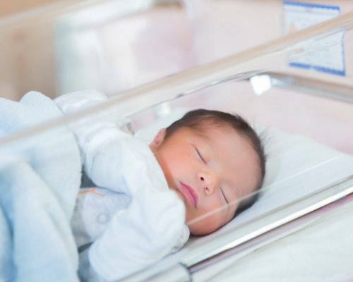 newborn baby sleeps in hospital crib in newborn clothes